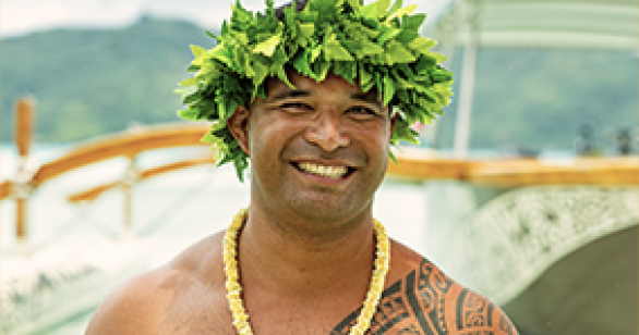 Tahitian man with green plant crown on head smiling directly at the camera with yellow flower necklace