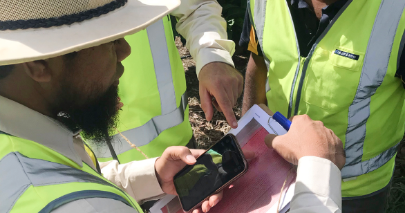 Farmers in green high vis holding a phone and a clip board